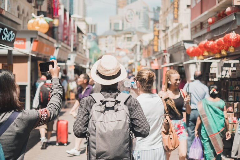 Vista desde atrás de un grupo de turistas caminando por una concurrida calle peatonal en un barrio asiático o Chinatown, decorada con farolillos rojos.